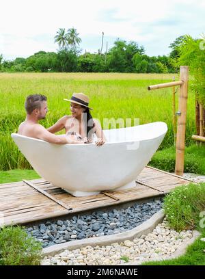 Männer und Frauen in der Badewanne draußen im Urlaub in einer Gastfamilie in Thailand mit grünem Reisfeld Stockfoto