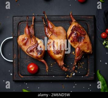 Das Frittieren der Wachtelkadaver liegt auf einem Holzbrett mit Gemüse Stockfoto