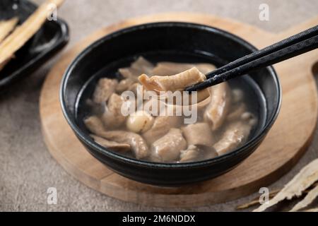 Four Tonics Suppe. Köstliches hausgemachtes taiwanesisches traditionelles chinesisches Kräutergericht mit Kräutern, Schweinedärm auf grauem Tischhintergrund Stockfoto