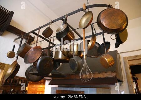 Antik aussehende Kupfer-, Messing- und eiserne Pfannen und Töpfe, die über dem Küchenherd hängen. Stockfoto