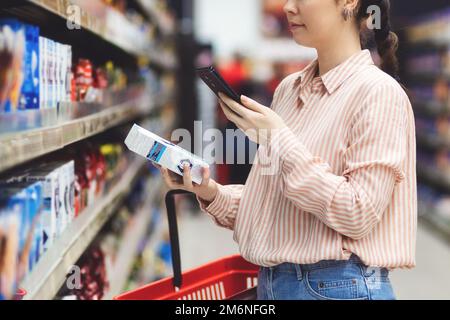 Nahaufnahme einer weißen Frau Scannen sie den qr-Code des Produkts mit dem Smartphone. Regale mit Lebensmitteln im Hintergrund. Kaufbegriff und Konsumerismus. Stockfoto