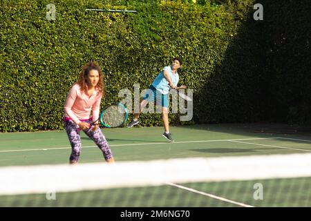 Biracial Paar spielt Tennis auf sonnigen Tennisplatz im Freien Stockfoto