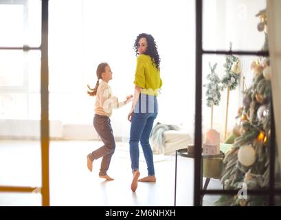 Glückliche Familienmutter und kleine Tochter, die Händchen hält und in einem hellen, sonnigen Raum tanzt Stockfoto