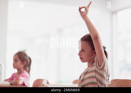 Das Mädchen hebt ihre Hand, während es an einem Projekt in einer modernen Vorschuleinrichtung teilnimmt. Selektiver Fokus Stockfoto