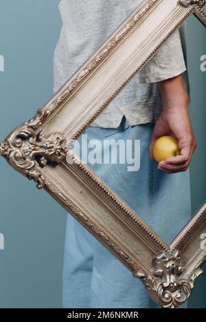 Junger Mann steht mit Bilderrahmen und Apfel im Studio. Stockfoto