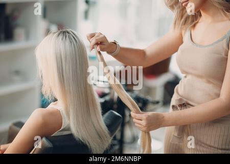 Friseur Frau macht Haarerweiterungen für junge Frau mit blonden Haaren im Schönheitssalon. Professionelle Haarverlängerung. Stockfoto