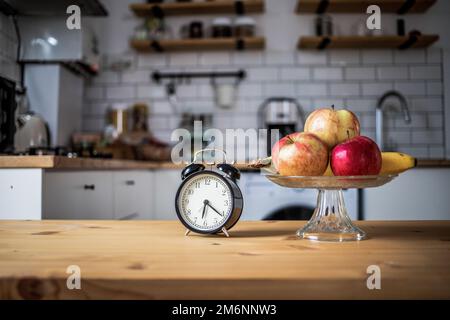 Klassischer Wecker und frisches Obst auf dem Küchentisch, zeitweiliges Fasten Stockfoto