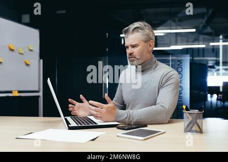 Unzufriedener, grauhaariger Chef im Büro, leitender Mann enttäuscht von dem erreichten Ergebnis, reifer Geschäftsmann verärgert und traurig, mit Dokumenten zu arbeiten und Laptop im Gebäude zu verwenden. Stockfoto