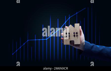 Die Hand hält ein hölzernes Modell eines Hauses auf dunklem Hintergrund. Immobilienverkauf Stockfoto