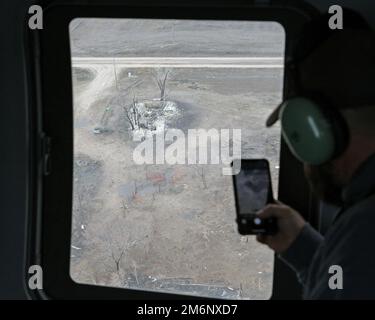 Feuerwehrchef Justin Mowry von der Wilsonville, Nebraska, Volunteer Fire Department beobachtet die Zerstörung eines ländlichen Bauernhofs durch das Fenster eines Nebraska Army National Guard UH-60 Black Hawk Helikopters und nimmt auf seinem Smartphone am 3. Mai 2022 in der Nähe von Cambridge, Nebraska, eine Aufnahme auf. Der Waldbrand der Road 702 entzündete sich am 22. April in Kansas und breitete sich schnell in Richtung Norden in den Grafschaften Furnas und Red Willow in Nebraska aus. Er wurde durch Dürre und starken Wind angefacht und brannte über 40.000 Hektar Land nieder, bevor er am 30. April durch Löschangriffe und Niederschläge vollständig gelöscht wurde. Stockfoto