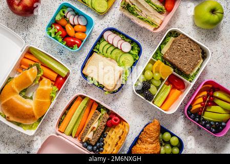 Aufnahme von Schullunchboxen mit verschiedenen gesunden, nahrhaften Mahlzeiten auf steinernem Hintergrund Stockfoto