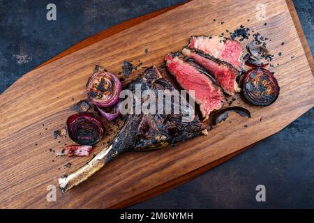 Traditionelles, trocken gereiftes Kobe Tomahawk Steak mit gegrillten Zwiebeln, serviert als Draufsicht auf einem Holzbrett Stockfoto