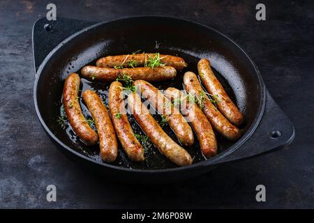 Traditionelle gebratene Bratwurst aus deutschem Schweinefleisch mit Kresse, serviert als Nahaufnahme in einer gusseisernen Pfanne auf einem rustikalen schwarzen Brett