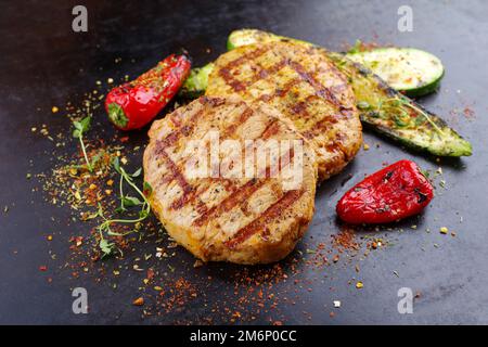Traditionelles Barbecue-Schweinefilet-Steak mit gegrilltem Gemüse und Gewürzen aus nächster Nähe auf einem alten rustikalen Brett Stockfoto