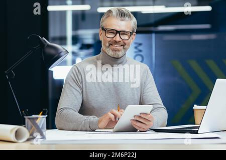 Porträt eines leitenden Architekten, grauhaariger Designer, der lächelt und in die Kamera schaut, Mann-Modell-Plan Verwenden Sie Laptop und Tablet-Computer bei der Arbeit im Studiobüro. Stockfoto