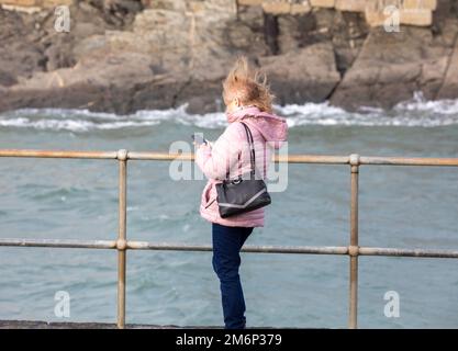 Porthleven, Cornwall, 5. Januar 2023, Eine Dame fotografiert mit ihrem Handy trotz des starken Windes in Porthleven, Cornwall. Die Temperatur lag bei 12C Grad, die Vorhersage ist für Regen und starke Winde für später heute. Kredit: Keith Larby/Alamy Live News Stockfoto
