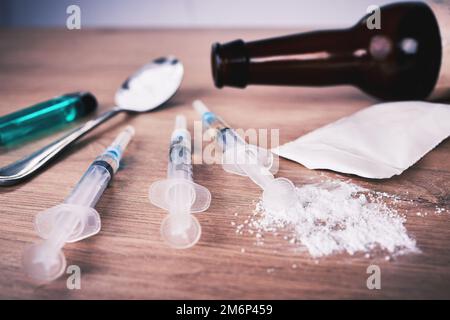 Pulver, Spritze und Medikamente mit Löffel auf dem Tisch bei Alkoholabhängigkeit, Drogenrehabilitation und Drogenmissbrauch. Medizin, illegale Produkte und Drogen Stockfoto