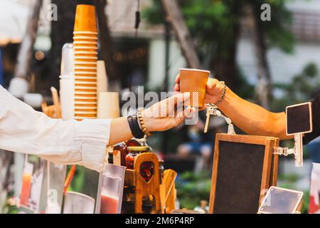 Ein Mann Barista serviert dem Gast heißen Kaffee in einem Pappbecher an der Theke im Café im Freien. Stockfoto