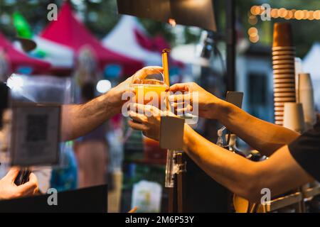Männlicher Barkeeper, der seinen Gästen ein heiliges Getränk in Plastikglas zum Mitnehmen serviert. Stockfoto
