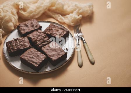 Hausgemachte Schokoladenbrownies auf weißem Teller auf beigefarbenem Hintergrund serviert Stockfoto