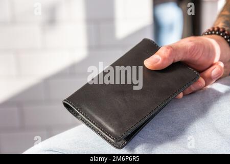 Migration und Unionsbürgerschaft. Die Hand des Mannes trägt einen Pass in schwarzem Lederbezug, Nahaufnahme. Handgefertigtes Zubehör. Konzept der Passkontrolle an der Grenze und Stockfoto