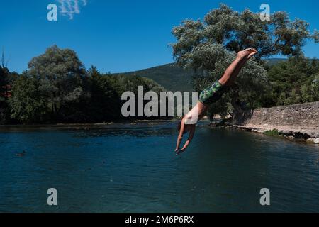 Junge Teenager springen fliegen und tauchen im Fluss. Klarer blauer Himmel und Bäume in der Ferne als natürlicher Hintergrund. Stockfoto