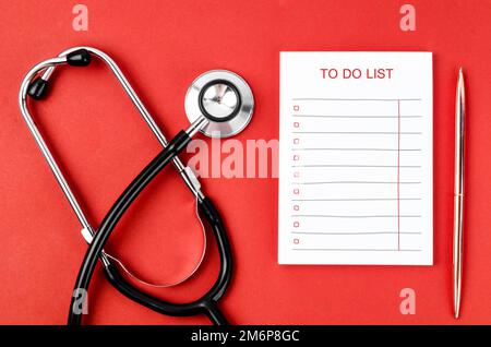 Leere Papiernotiz To-do-Liste oder Wunsch und Stethoskop mit medizinischem Stift auf rotem Hintergrund. Stockfoto