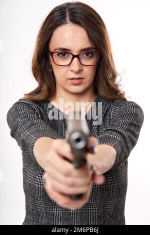 Geschäftsfrau in Lesebrille mit ernstem Ausdruck, die eine Waffe auf die Kamera richtet, isoliert auf weißem Hintergrund Stockfoto