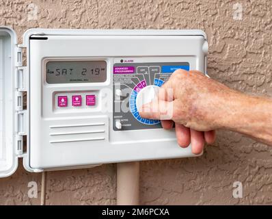 Automatischer Timer für die elektrische Außenbewässerung. Nahaufnahme des programmierbaren Rasenbewässerungssystems mit männlicher Hand. Stockfoto