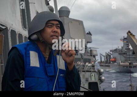 PHILIPPINE SEA (3. Mai 2022) Seemann Julian Monsanto aus Las Vegas kommuniziert mit einem schallbetriebenen Headset mit der Brücke an Bord des Arleigh Burke-Klasse-Guided-Missile Destroyer USS Dewey (DDG 105) während einer Wiederauffüllung auf See mit dem Henry J. Kaiser-Class-Nachfüllöler USNS Tippecanoe (T-AO-199). Dewey ist dem Kommandeur, der Task Force 71/Destroyer Squadron (DESRON) 15, der größten nach vorn eingesetzten DESRON der Marine und der Hauptstreitkräfte der US-7.-Flotte zugewiesen. Stockfoto