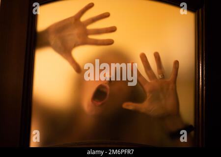 Gruseliges Bild von Händen hinter Glas, Horror-Geisterfrau hinter der Tür, Halloween-Konzept Stockfoto
