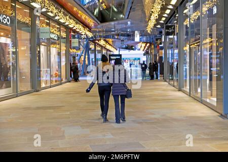 Rückansicht zwei junge weibliche Käuferinnen, die an Geschäften im leeren Einkaufszentrum One New Change in London, England, vorbeilaufen, KATHY DEWITT Stockfoto