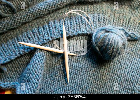 Kreisförmige Stricknadel auf dem Hintergrund eines blauen Wollknäuels aus Wolle handgestrickter Pullover Wales UK KATHY DEWITT Stockfoto