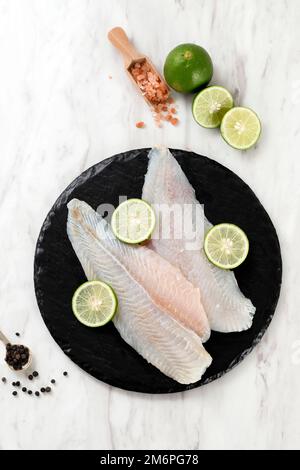 Rohes Pangasius auf einem Schneidebrett mit Blackpepper und Salz auf weißem Marmorhintergrund Nahaufnahme Stockfoto