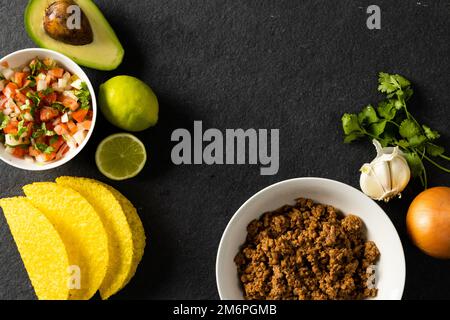 Direkt über Schuss von Tortillas, Fleisch, Avocado, Zitrone, Koriander, Zwiebel, Tomaten und Knoblauch auf dem Tisch Stockfoto