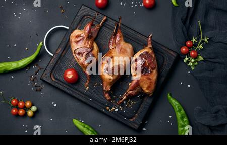 Das Frittieren der Wachtelkadaver liegt auf einem Holzbrett mit Gemüse Stockfoto