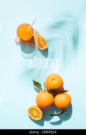Orangenobst mit Scheiben und einem Glas Saft auf blauem Hintergrund mit Sonnenlicht. Stockfoto