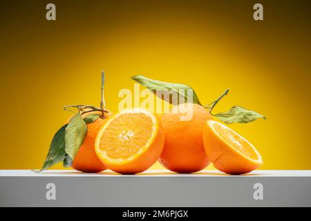 Frische Orangenfrüchte mit Blättern auf gelbem Hintergrund. Stockfoto