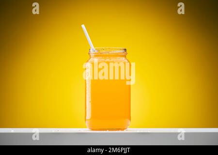Frischer Orangensaft im Glasbehälter auf gelbem Hintergrund. Stockfoto