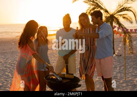 Gemischte Rennfreunde beim Grillen am Strand Stockfoto