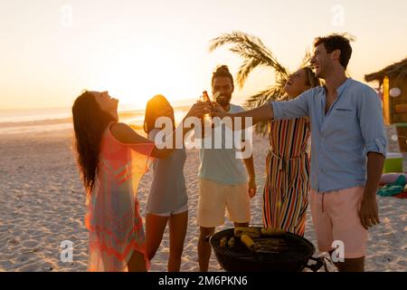 Gemischte Rennfreunde beim Grillen und Alkohol am Strand Stockfoto