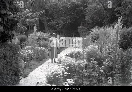 1950er, historisch, eine ältere Besucherin in den Gärten von Ann Hathaways Cottage, einem strohgedeckten Bauernhaus in Shottery, Warwickshire, England, Großbritannien, die Kindheit der Frau des berühmten englischen Dramatikers William Shakespeare, der in der nahe gelegenen Stadt Stratford-upon-Avon geboren wurde. Stockfoto