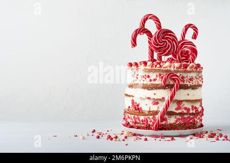Weihnachten viele Schichten Kuchen dekoriert mit Lolli-Pops, rot-weiße Konfetti auf weißem Kuchenständer, Weihnachtsbälle, Tannenzweige auf weißem Betontisch Stockfoto