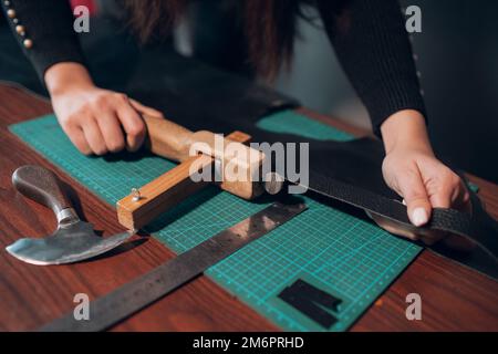 Tanner Frau schneidet Lederwaren in der Werkstatt. Arbeitsprozess des Lederhandwerks Stockfoto