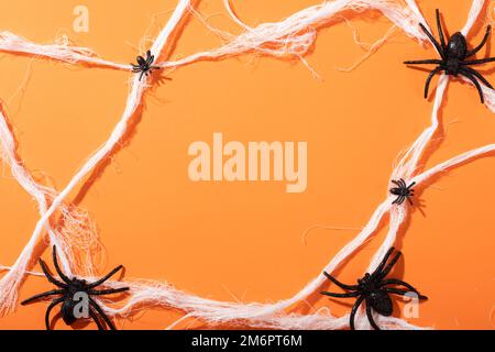 Mehrere Spider-Spielzeuge bilden ein Spinnennetz mit Kopierraum vor orangefarbenem Hintergrund Stockfoto