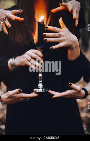 Hexe mit brennender Kerze, die während eines magischen Rituals im dunklen Herbstwald von vielen Händen berührt wird Stockfoto