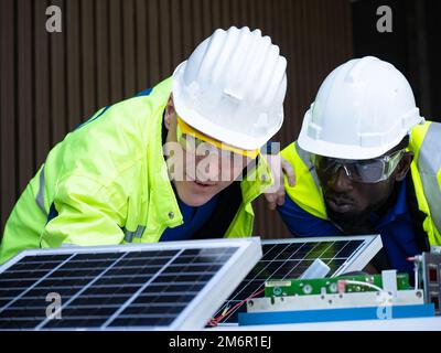 Zwei professionelle Solarzelleningenieure mit Schutzweste und Schutzhelm testen das Solarzellenmodul. Der Techniker prüft die Wartung Stockfoto