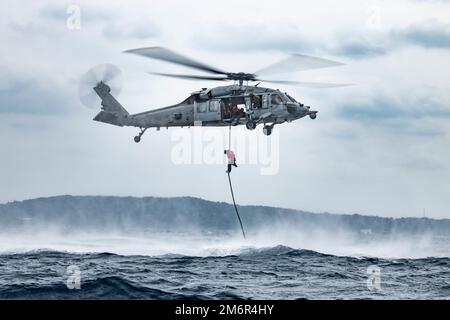 EIN US-AMERIKANISCHER Navy MH-60 Sea Hawk Helicopter, dem Helicopter Sea Combat Squadron 85 zugeteilt, hostet eine US Luftwaffe-Sanitäter, der 320. Spezialtaktik-Staffel, über Wasser zugeteilt, während eines Trainings in der White Beach Naval Facility, Japan, 4. Mai 2022. Das Team hat geübt, Kampfgummi-Razzien aus einem US-Staat zu werfen Navy MH-60 Sea Hawk Helikopter, springt hinterher und baut die CRRC nach der Landung im Wasser zusammen. Stockfoto