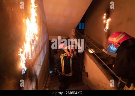 Der mutige Feuerwehrmann steigt die Treppe eines brennenden Gebäudes hinab und hält das errettete Mädchen in seinen Armen. Feuer eröffnen und ein Feuerwehrmann im Rücken Stockfoto