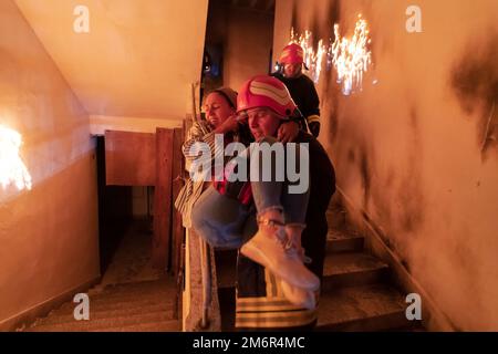 Der mutige Feuerwehrmann steigt die Treppe eines brennenden Gebäudes hinab und hält das errettete Mädchen in seinen Armen. Feuer eröffnen und ein Feuerwehrmann im Rücken Stockfoto